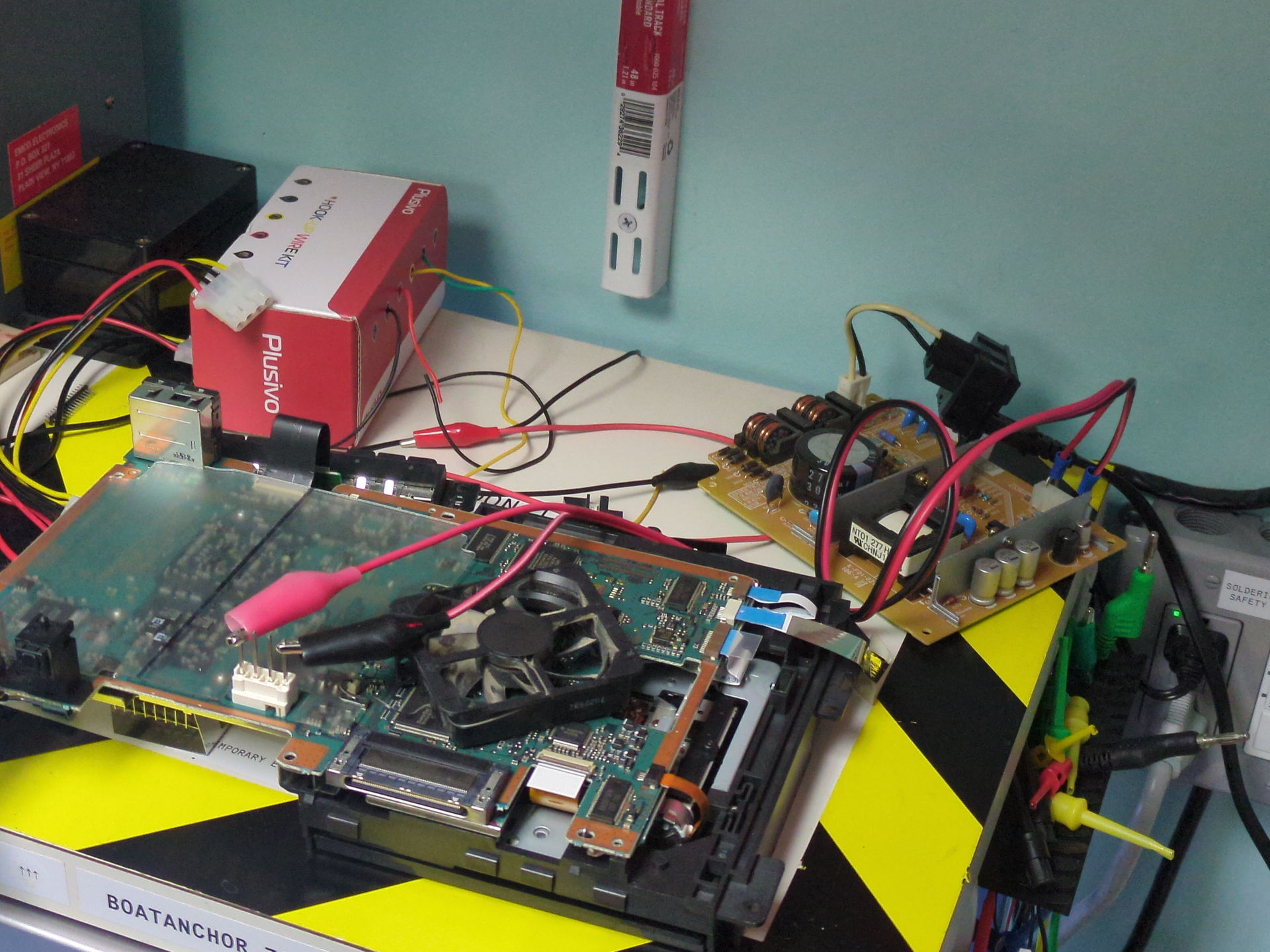 A stripped down PS2 laid out on a shelf with the power supply connected with alligator clips